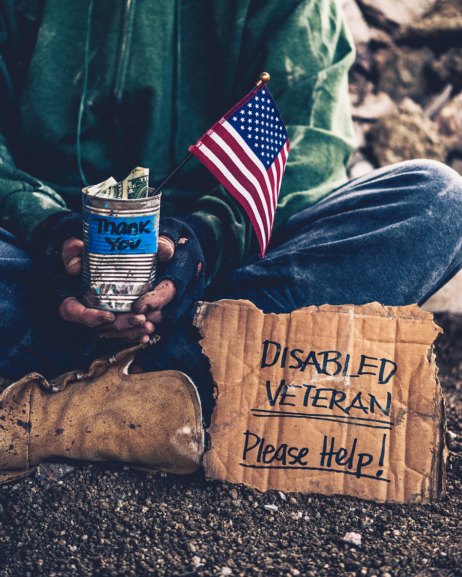 Fighting adversity. Homeless disabled veteran with sign and money tin